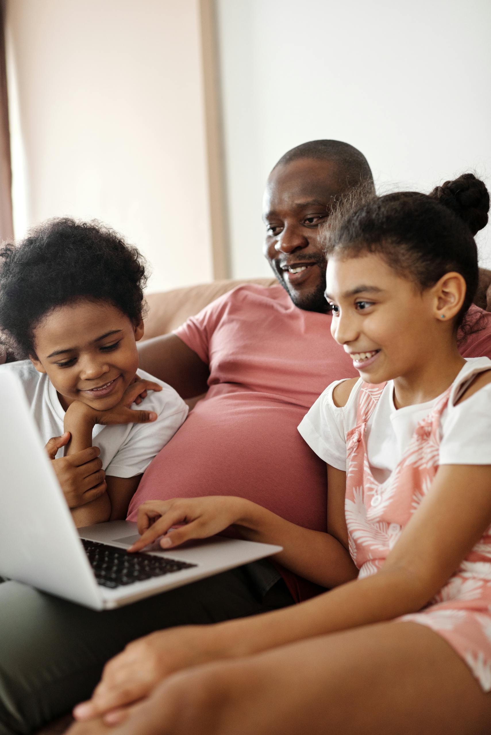 Smiling father and kids using a laptop at home, sharing joyful moments.